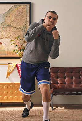 Man in gray hoodie and blue shorts posing in a room with a map and couch.